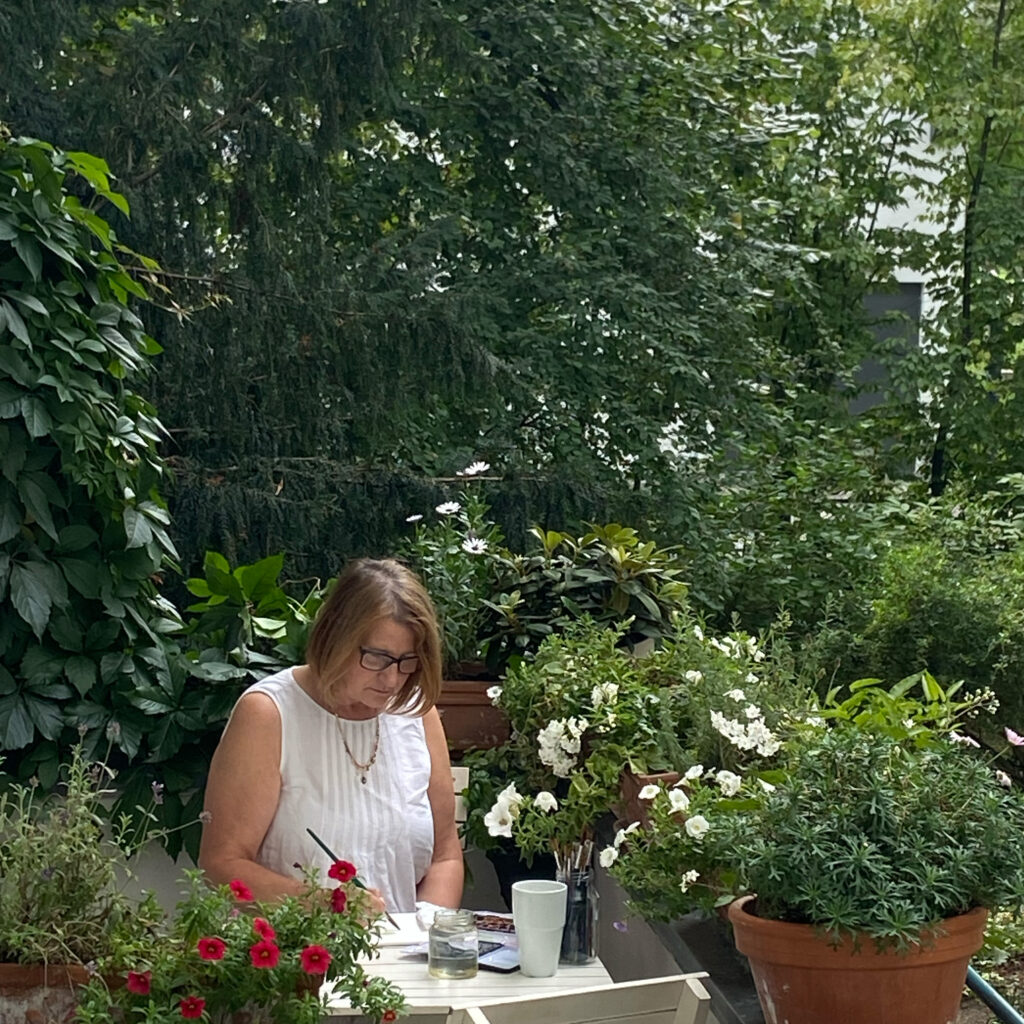 frau brandt works as an illustrator and paints on her balcony in summer